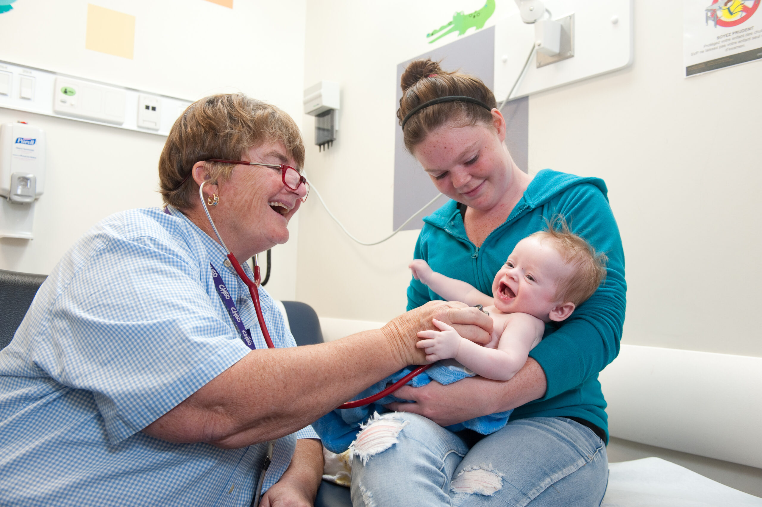 A female doctor smiles at her infant patient who is held by her yooung mother.